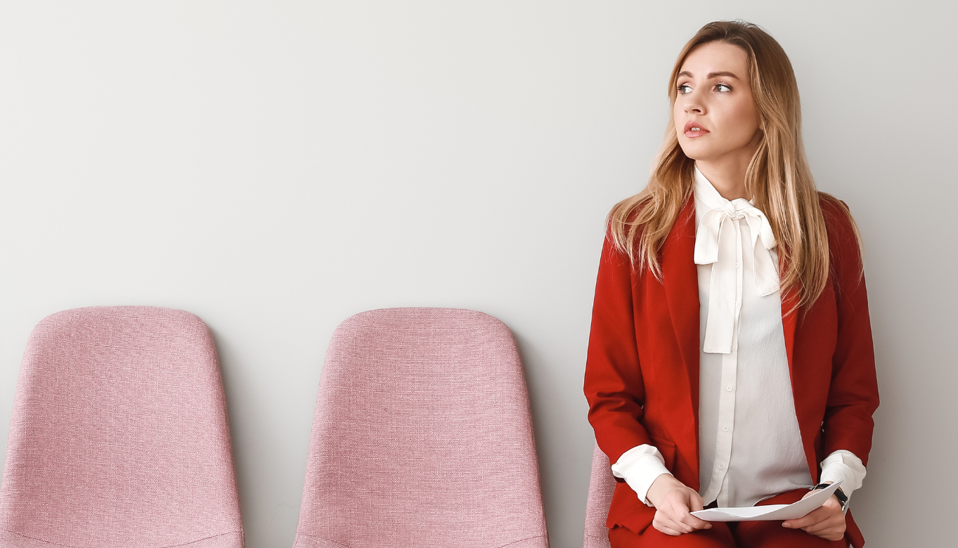 An image of a blonde-haired woman wearing a red suit sitting in a pink chair holding her resume